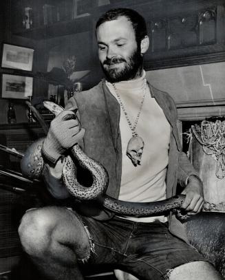 Norman Elder holds 7-FT. Anaconda he brought from Peru. Around his neck is a monkey skull on a necklace of beads
