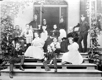A posed informal group shot of the Frederic Charles Denison family: He sits at left in a wooden…