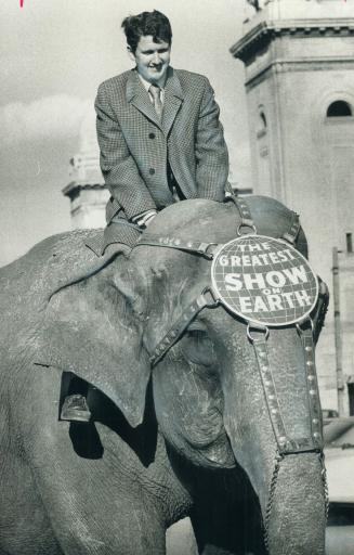 Just along for the ride, reporter George Gamester hangs onto Poopsie, a 7,000-pound elephant that earns her living by performing for the Ringling Brot(...)