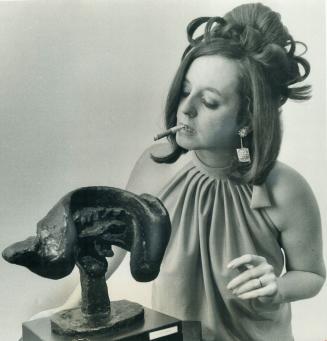 Toronto sculptors wife, Mrs. Gerald Gladstone, wreathers the Lipchitz Head of Harlequin in cirgar smoke. Most of the sculptures on display at the new (...)