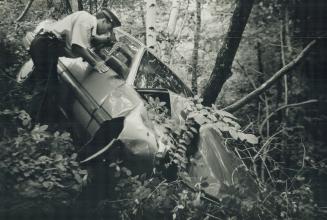 Stolen car dumped off bluffs, Metro police Constable Cory McKnight checks a 1989 Audi yesterday after the car, reported stolen, was found pushed over the ledge of the Scarborough Bluffs