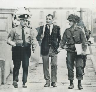 Sharing their guard duties, a Montreal city policeman, a detective in plain clothes and a uniformed soldier from the Van Doos regiment, wearing a camo(...)
