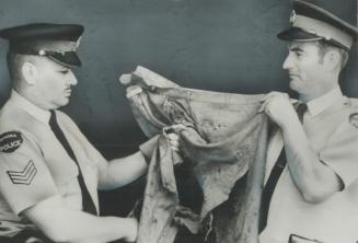 Kenora Policemen-Sgt. Robert Letain (left) and Constable Donald Milliard-examine pants Milliard was wearing when a bank robber was blown up by sticks (...)