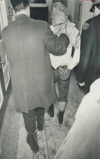 Wearing leg chain, and with his hands handcuffed behind his back, bank robbery suspect is led away by policemen
