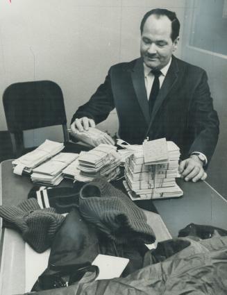 $6,744,170.35 worth of Cheques and money orders, stolen yesterday in Mettro's biggest bank haul in 20 years, are examined by Detective Sgt. Ken Wilkin(...)