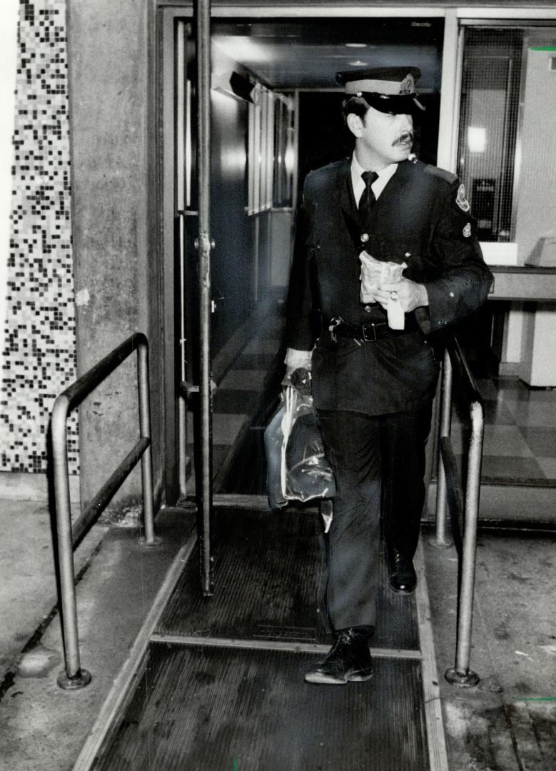 Constable's clothes: A policeman carries the uniform and other articles worn by the wounded Constable Glen Bacon from Wellesley Hospital