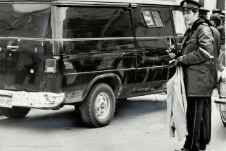 Bullet-ridden van: Policeman holds the jacket discarded by bank robber who got away in Yorkville after police chased him and two accomplices in the black van shown in background