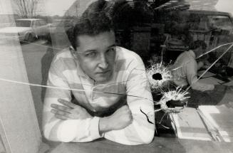 Scary view: Terry Clarke, 28, a draftsman for Durham Region, looks out two window panes shattered by a bullet that ended up lodged in his files yesterday