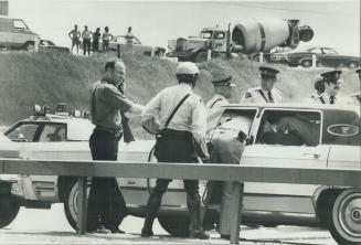 Wounded man inside car with U.S. license plates is examined by police today after a 100 m.p.h. chase along Highways 400 and 401. The man was shot thre(...)