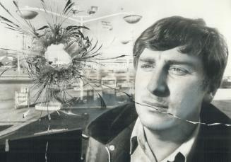 Bullet hole in garage window is studies by mechanic Larry Cave