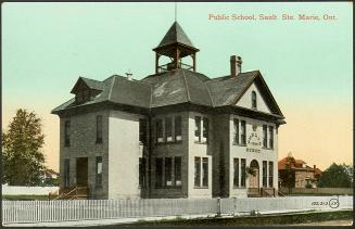 A two-storey white building, with a bell in an open tower, surrounded by a white picket fence. …