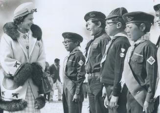 Queen Elizabeth the second in large coat smiles at line of boy scouts in black and white photo