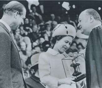 At Kelowna, B.C., Queen Elizabeth and Prince Philip admire a glass-enclosed sculpture presented to them by Mayor Hilbert Roth (right) during their vis(...)