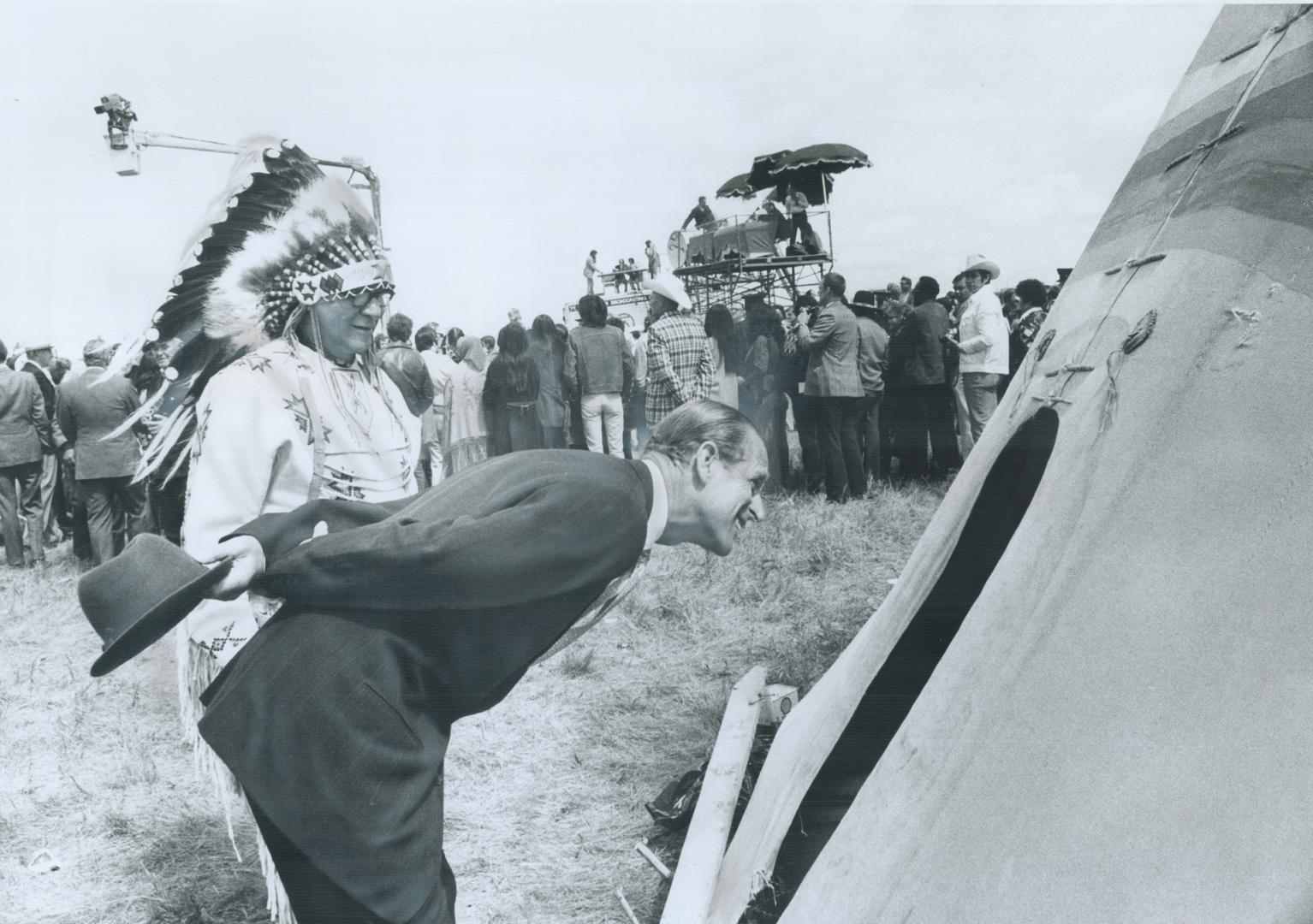 Tall Prince Philip leans over to peer into a teepee in an Indian village at Calgary, which he and the Queen visited before she opened the Calgary Stam(...)
