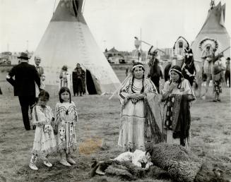 Dressed in fringed and beaded tribal costumes, Indian women and children await the coming of the King and Queen to Calgary, where an encampment was se(...)