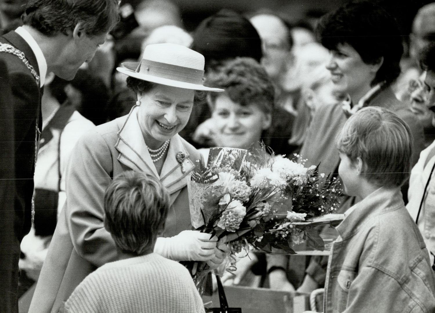 Queen accepting flowers from kids during her walkabout in downtown Vancouver followed by Mayor Gordon Campbell
