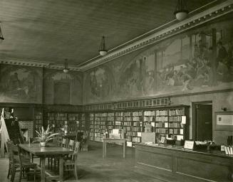 Image shows an interior of the library branch with a desk on the right, book stacks along the w ...