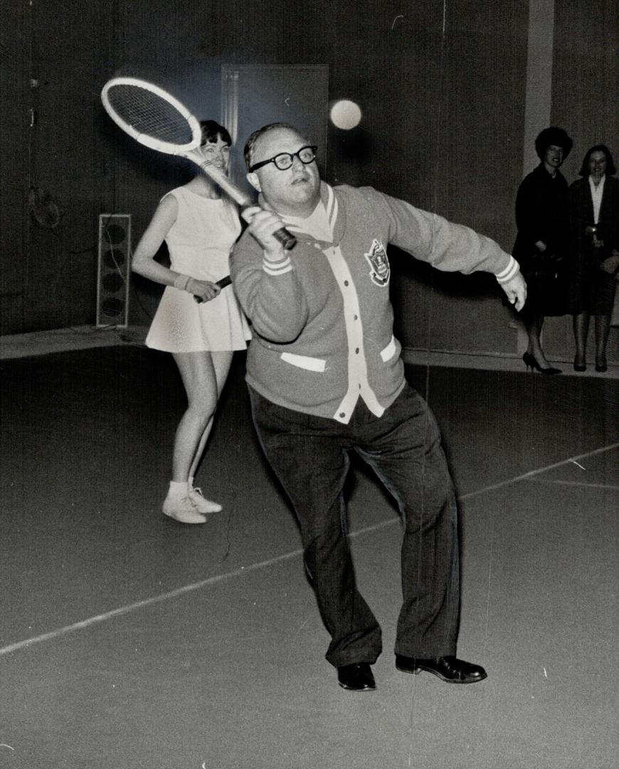 In which he serves. Mayor Givens is backed up by Mrs. H. Goulding as he opened York Racquets Club on Yonge St., Toronto's first club built specifically for indoor tennis