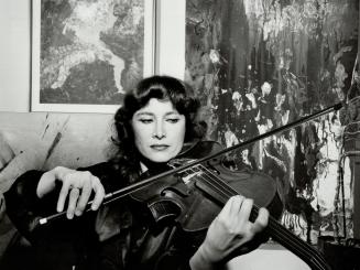 Rivka Golani-Erdesz, Viola player in action in her home with some of her paintings in the background