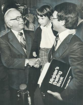 Taking over as minister of consumer and commercial relations last month, Larry Grossman, with son Jamie, is congratulated by his father Allan Grossman(...)