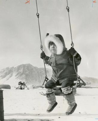 Native Youngster, swinging in the winter, illustrates combination of old ways and new which already characterizes Canada's North
