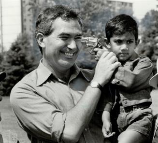 Laughing man holds young child, who presses toy pistol to the man's temple.