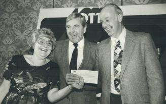 Image shows two lottery winners holding a check. The Minister is standing on the right.