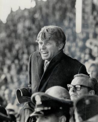 An argo fan, Senator Robert Kennedy leaps to his feet to cheer during a tight moment in Sunday's tie game with Ottawa Rough Riders at the CNE stadium.(...)