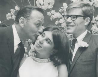 A kiss from a comedian. Track star Bruce Kidd beams as his new bride, the former Varda Burston, gets a kiss from her uncle, comedian Frank Shuster. Th(...)