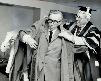 After receiving an honorary degree yesterday from York University, John Yolton, acting president of York, is helped into his robes by Chancellor Walte(...)