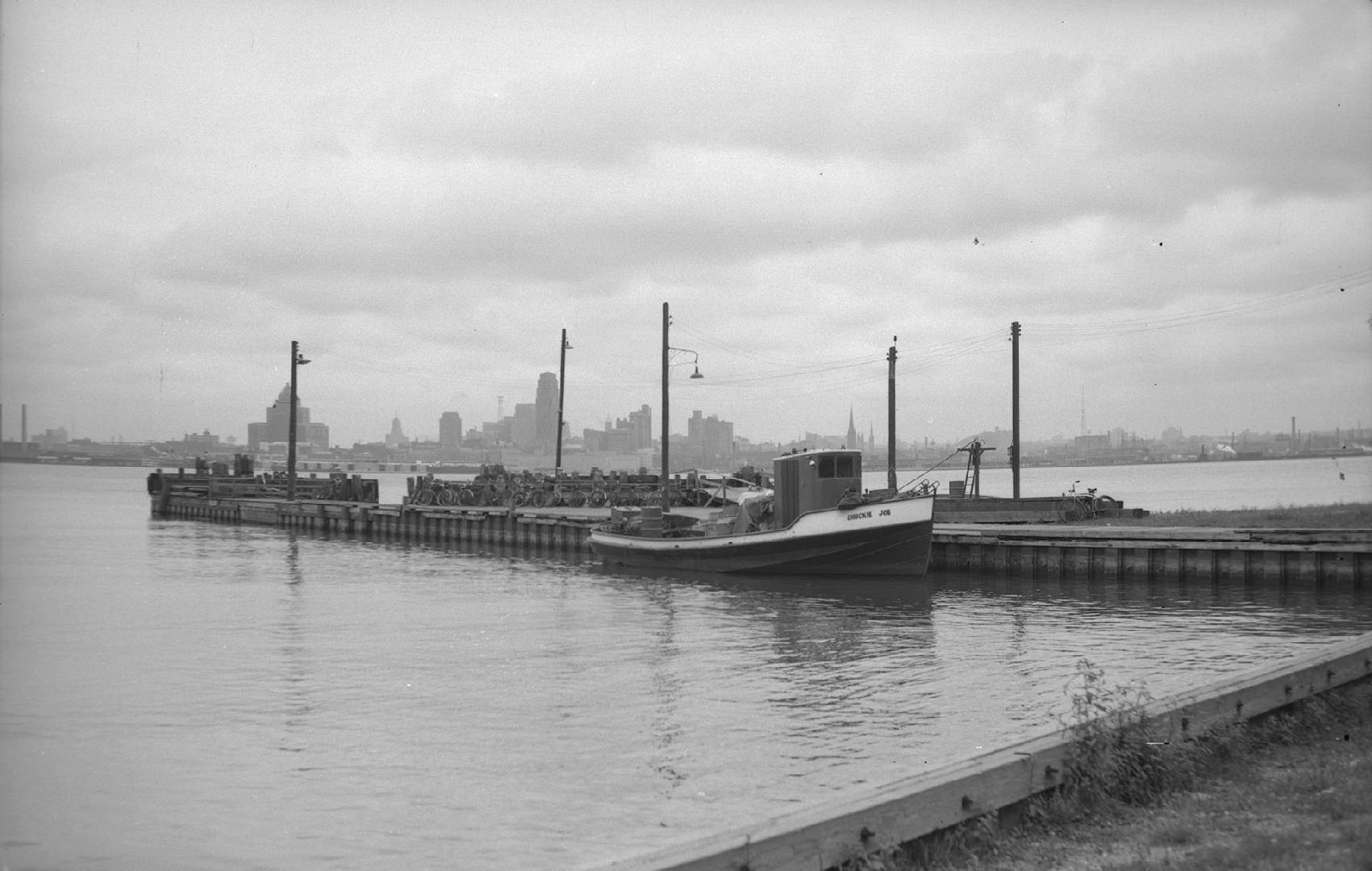 Image shows a tugboat docked at the island with the Toronto Harbour in the background.