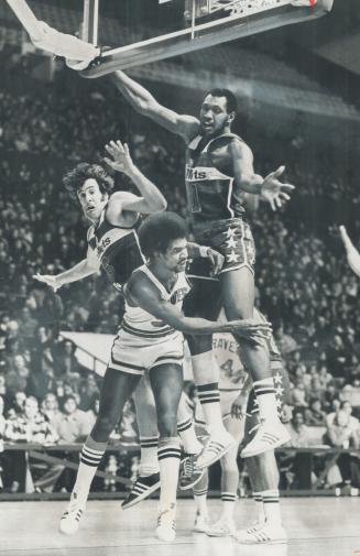 In a ballet-like movement, Buffalo braves' Randy Smith has flicked ball to a teammate, while Elvin Hayes (6) and Mike Riordan of Capital Bullets tower(...)