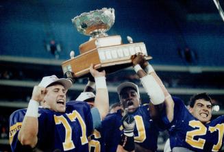Championship form: That's the Vanier Cup being hoisted by members of Wilfrid Laurier Golden Hawks, Linebacker Fred Grossman (left), defensive back Lonny Taylor and running back Andy Cecchini (right)