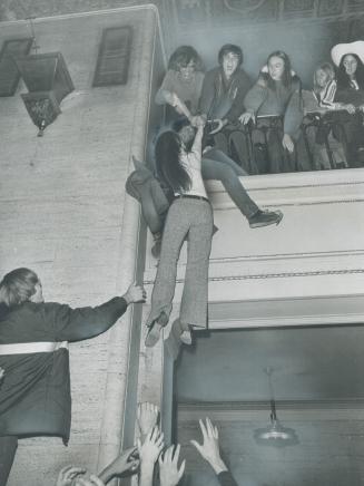 On her way up to greet friends - or whoever may be there - a girl makes the trip from lobby to mezzanine the hard way, pulled by two youthful Grey Cup(...)