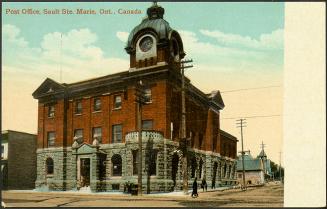 A three-storey stone and brick building with an imposing clock tower on the corner of an unpave…