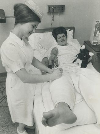 Hey, that's not my chart. Nancy McCredie, in Toronto General hospital bed following knee surgery, watches as nurse Sandra Shantz takes time out from m(...)