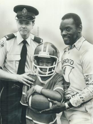 Easing tensions. Metro police Constable Joe Keast and Toronto Argonaut star running back Terry Metcalfe give a few pointers to 12-year-old Paul Spence(...)