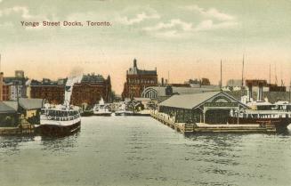 Image shows a few boats by the wharf and a number of waterfront buildings.