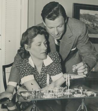 George Murphy, talented actor, examines a tiny pitcher from his wife's set of miniature silver