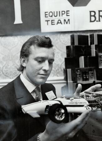 Racing driver Jackie Oliver holds model of his Grand Prix car as he stands in front of a display of cologne, aftershave and talcum powder. Yardley cos(...)