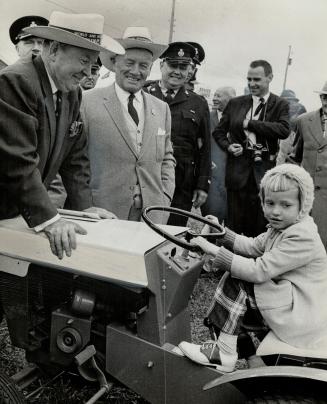 Pert plowgirl. Perched on the seat of a small tractor, four-year-old Linda Disher of Wellandport meets Prime Minister Lester Pearson (left) and Conn S(...)