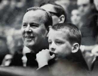 Taking time out from political activities, Liberal Leader Lester Pearson and his 8-year-old grandson, Paul Hannah, watch Maple Leafs - and Liberal M.P(...)