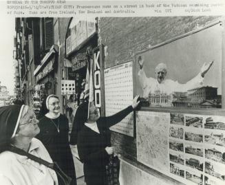 Franciscan nuns on a street in back of the Vatican examining poster of Pope
