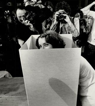 Margaret Trudeau voting with husband peeks above voting booth while surrounded by photographers on all sides