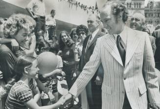 Arriving at Nathan Phillips Square, Prime Minister Pierre Trudeau smilingly shakes hands with a little girl reaching out from the crowd