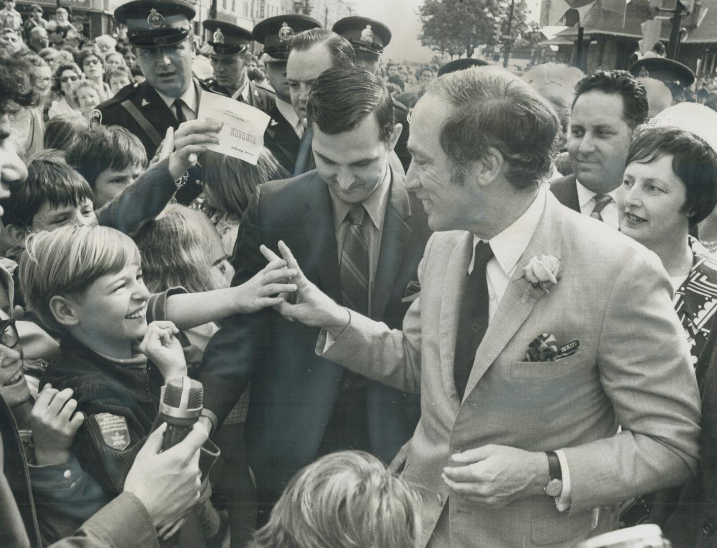Mobbed by school children as he arrives at Guelph City Hall today Prime Minister Pierre Trudeau flashes a V sign and says Peace to the youngsters. The(...)