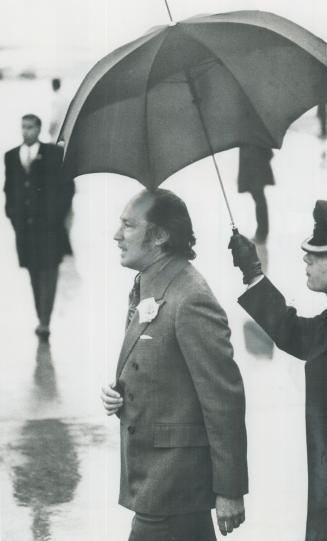 Shielded from 32-degree drizzle of snow and rain, Prime Minister Pierre Trudeau walks across the airport to greet U
