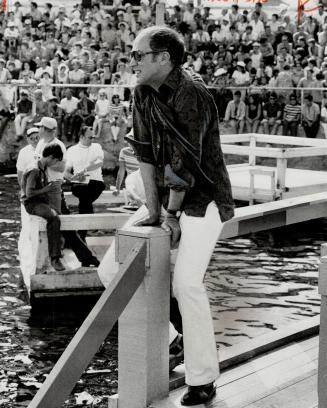 Down on a pier with Pierre. Prime Minister Pierre Trudeau dangles his legs over floating platform's guardrails after finishing impromptu jig for a crowd in Quebec's Lac St. Jean region Saturday