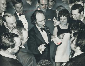 Surrounded by wellwishers, Prime Minister Pierre Trudeau carries pen in mouth so he can shake hands with guests who paid $50 each to dine with him at Royal York Hotel last night