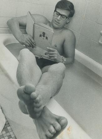 Herman Willemse, favorite in today's CNE marathon swim, relaxes in bathtub prior to, race with book mysterious Strength in Sport